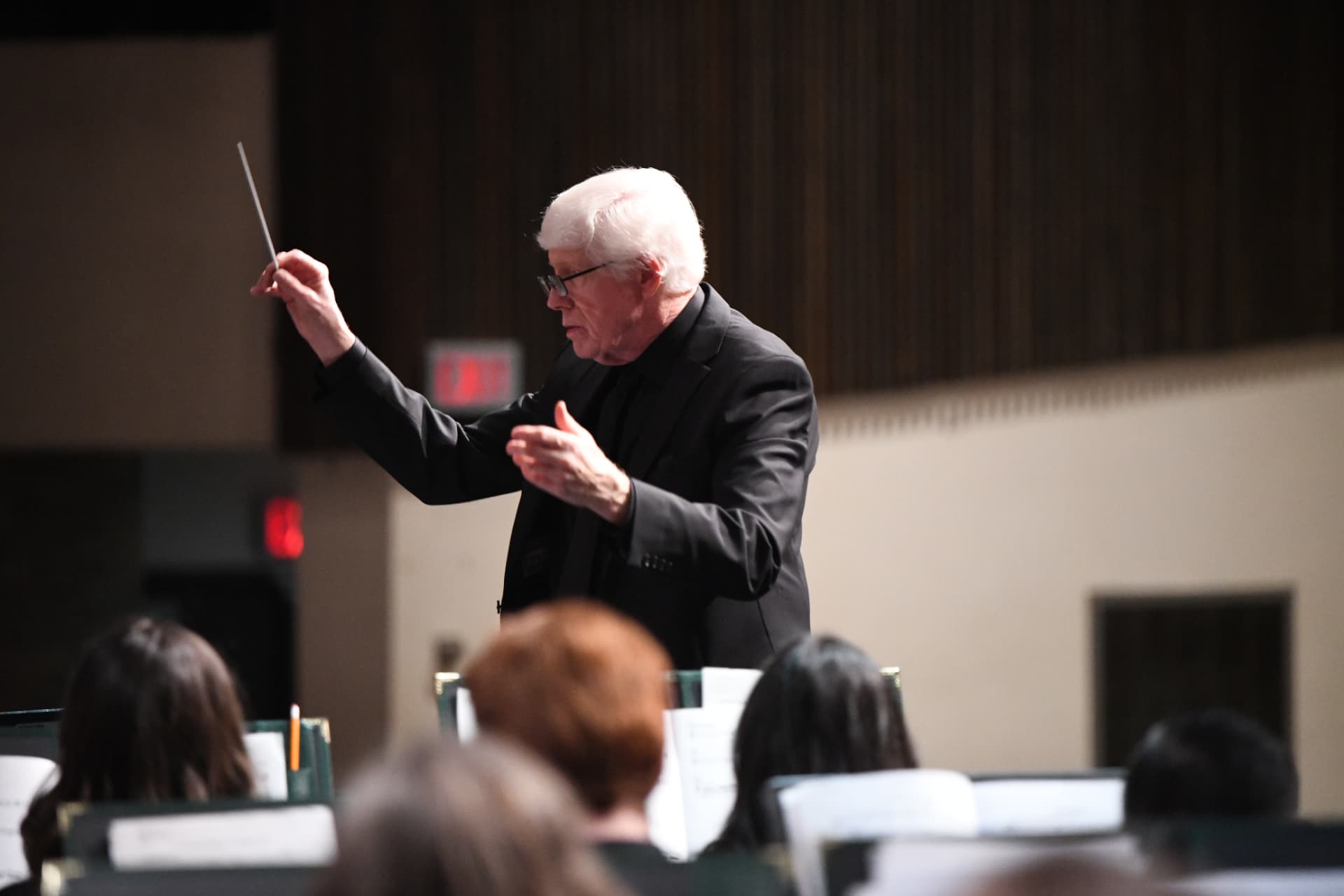 The conductor, baton in hand, leading the ensemble from behind the podium