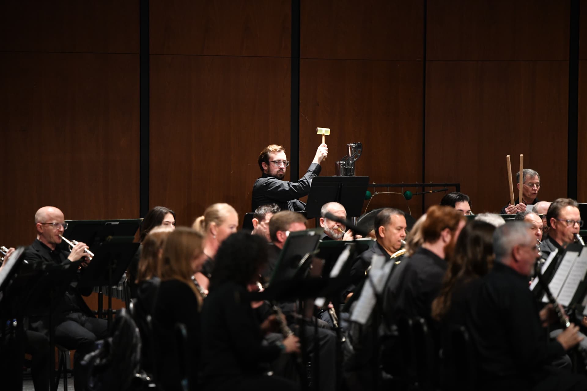 A percussionist striking the tubular chimes surrounded by flutes and clarinets